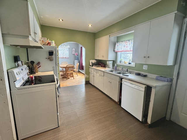 kitchen with arched walkways, light countertops, white cabinetry, a sink, and white appliances