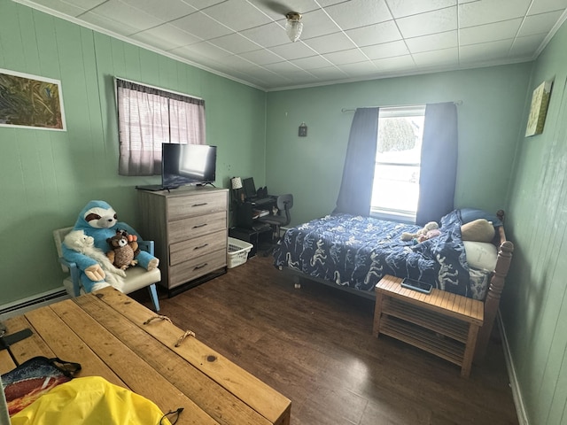 bedroom with ornamental molding, a baseboard heating unit, and wood finished floors