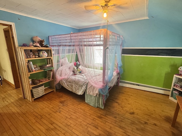 bedroom featuring a baseboard heating unit, wood-type flooring, crown molding, and a ceiling fan