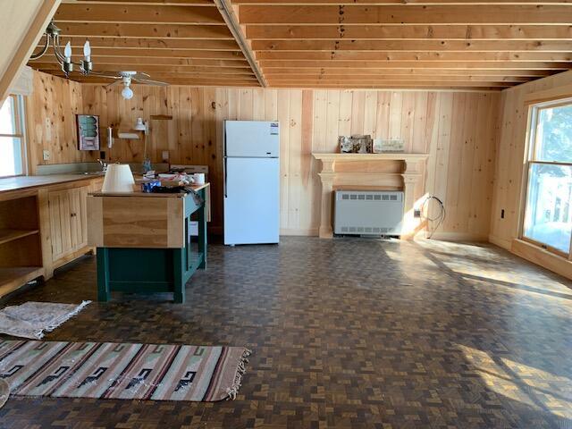 kitchen with radiator, a fireplace, wood walls, and freestanding refrigerator