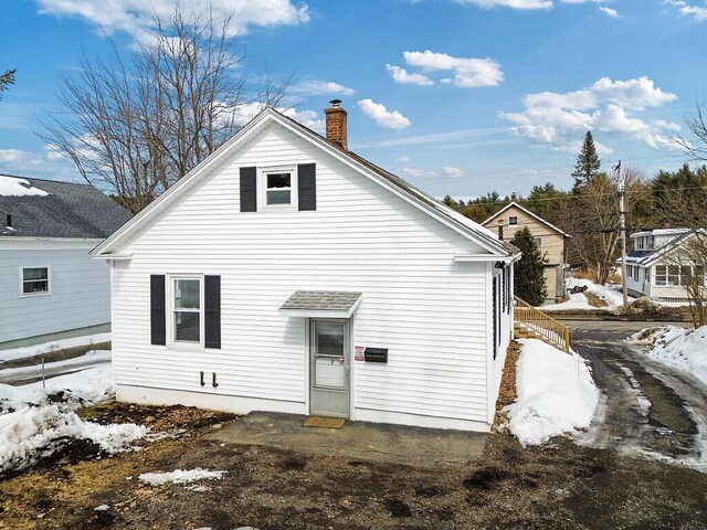 snow covered rear of property featuring a chimney