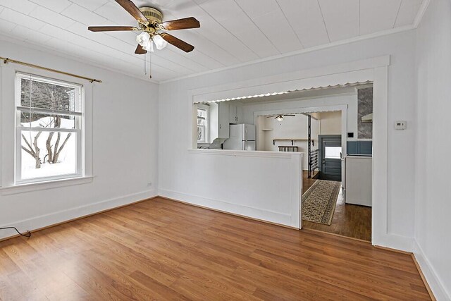 empty room with baseboards, wood finished floors, a ceiling fan, and crown molding