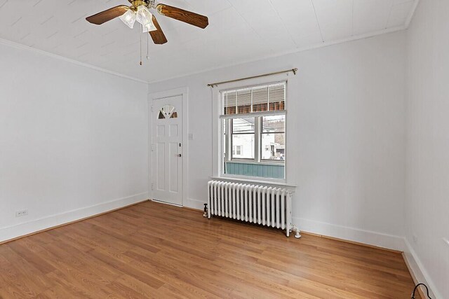 empty room featuring light wood-style floors, radiator, crown molding, and baseboards