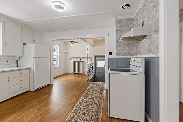 kitchen featuring under cabinet range hood, white appliances, wood finished floors, visible vents, and radiator heating unit