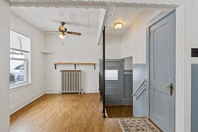 entrance foyer featuring light wood-style flooring, radiator heating unit, a ceiling fan, baseboards, and stairs