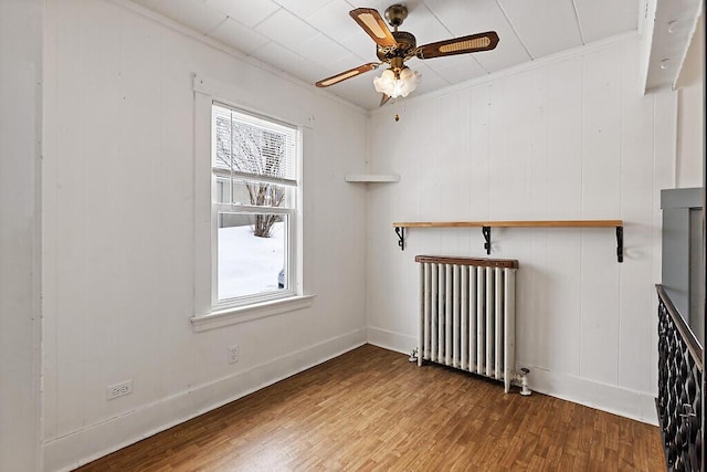 spare room featuring radiator heating unit, a ceiling fan, wood finished floors, and ornamental molding