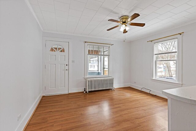 entryway with baseboards, crown molding, light wood-style flooring, and radiator heating unit