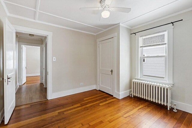 unfurnished bedroom with baseboards, a ceiling fan, radiator, hardwood / wood-style flooring, and ornamental molding