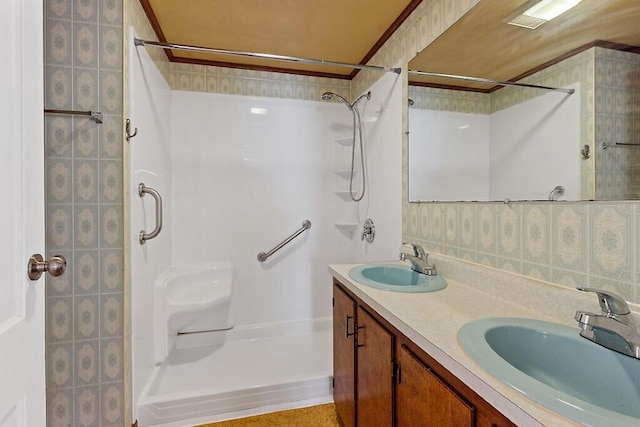 bathroom featuring a stall shower, double vanity, a sink, and wallpapered walls