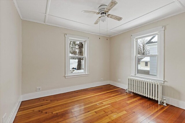 spare room with baseboards, ceiling fan, hardwood / wood-style floors, and radiator heating unit