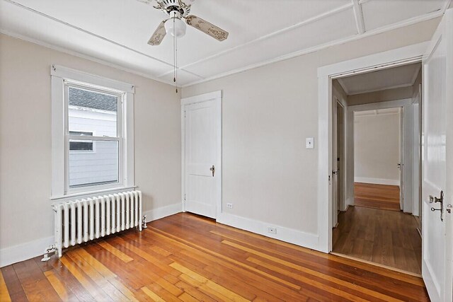 spare room featuring a ceiling fan, baseboards, hardwood / wood-style floors, and radiator heating unit