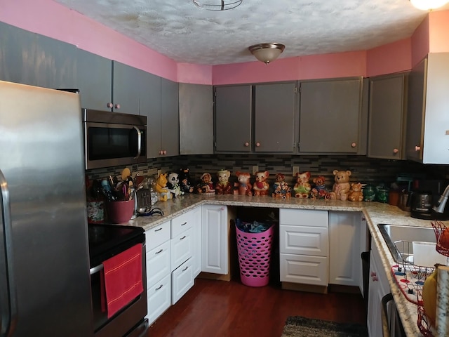 kitchen featuring light stone counters, a sink, appliances with stainless steel finishes, dark wood-style floors, and tasteful backsplash