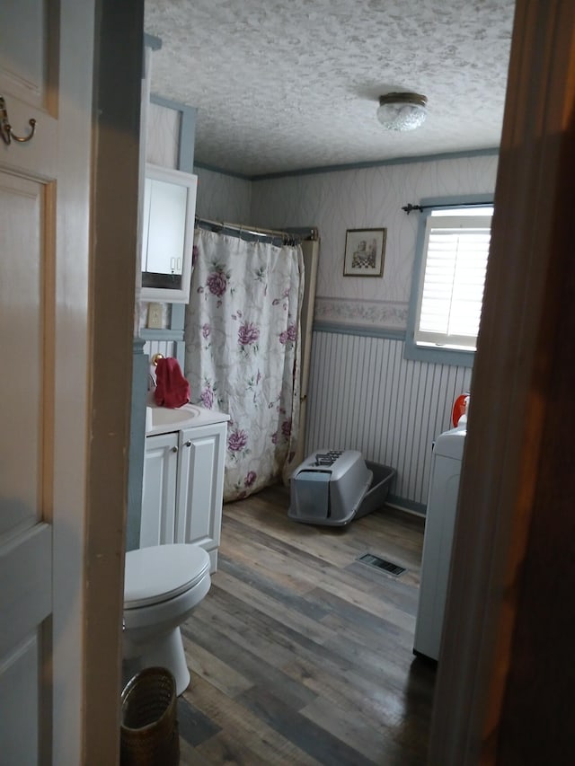 full bathroom featuring a textured ceiling, toilet, wood finished floors, a shower with curtain, and washer / clothes dryer