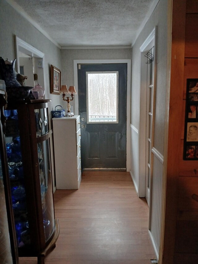 doorway featuring light wood-style floors, ornamental molding, and a textured ceiling