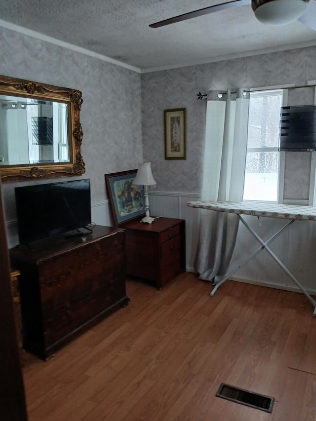 unfurnished office featuring crown molding, visible vents, light wood-style floors, ceiling fan, and a textured ceiling