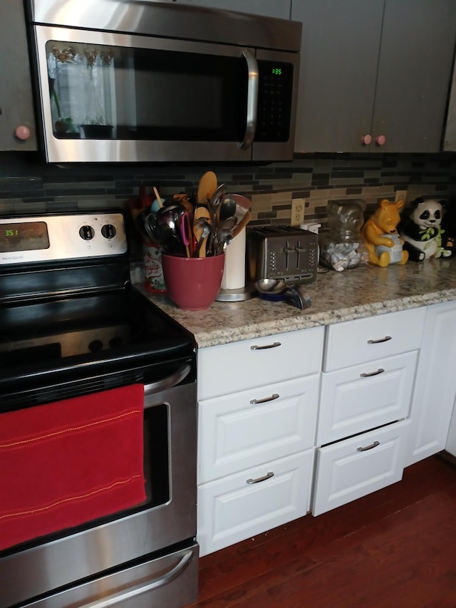 kitchen featuring light stone counters, stainless steel appliances, dark wood-type flooring, white cabinetry, and decorative backsplash