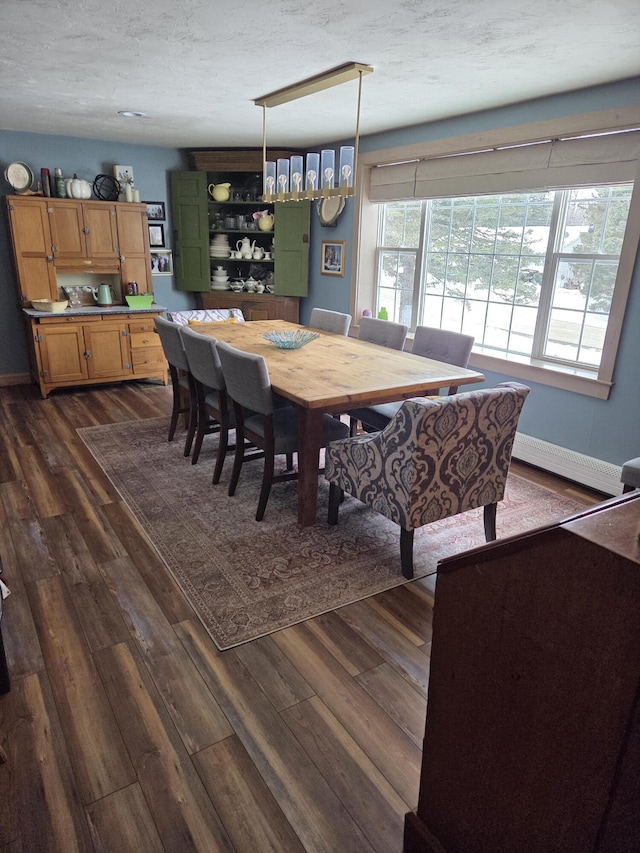 dining space featuring a baseboard heating unit, a textured ceiling, dark wood finished floors, and baseboards