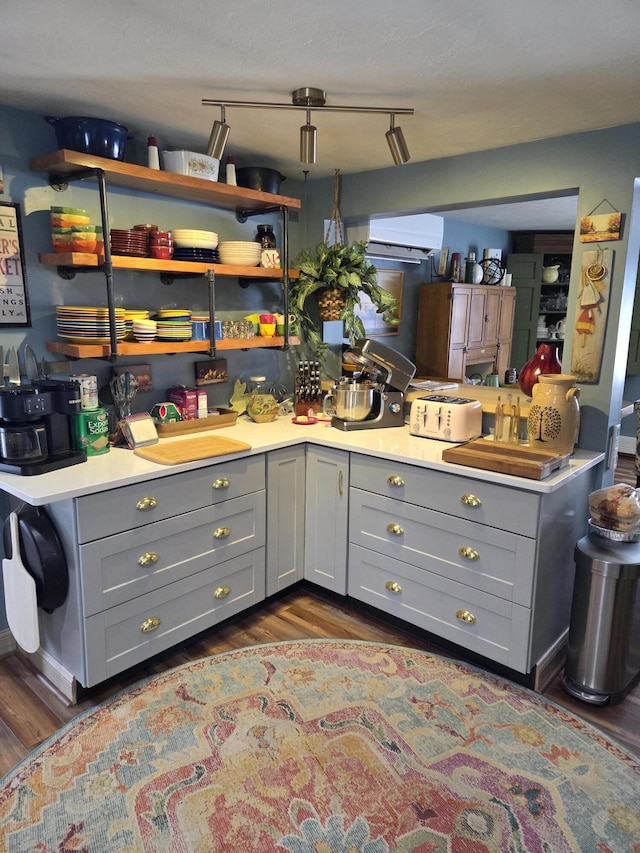 kitchen with dark wood finished floors, light countertops, gray cabinetry, a wall mounted AC, and a peninsula