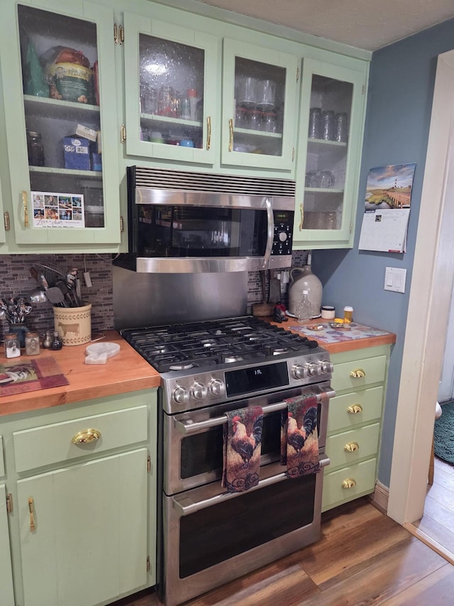 kitchen with stainless steel appliances, wood finished floors, tasteful backsplash, glass insert cabinets, and green cabinetry