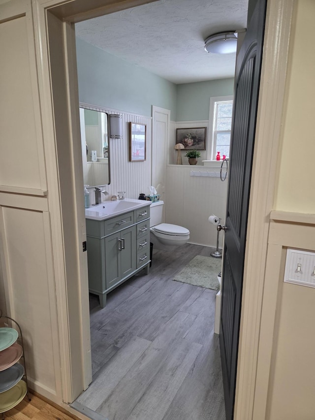 bathroom with toilet, a textured ceiling, wood finished floors, and vanity