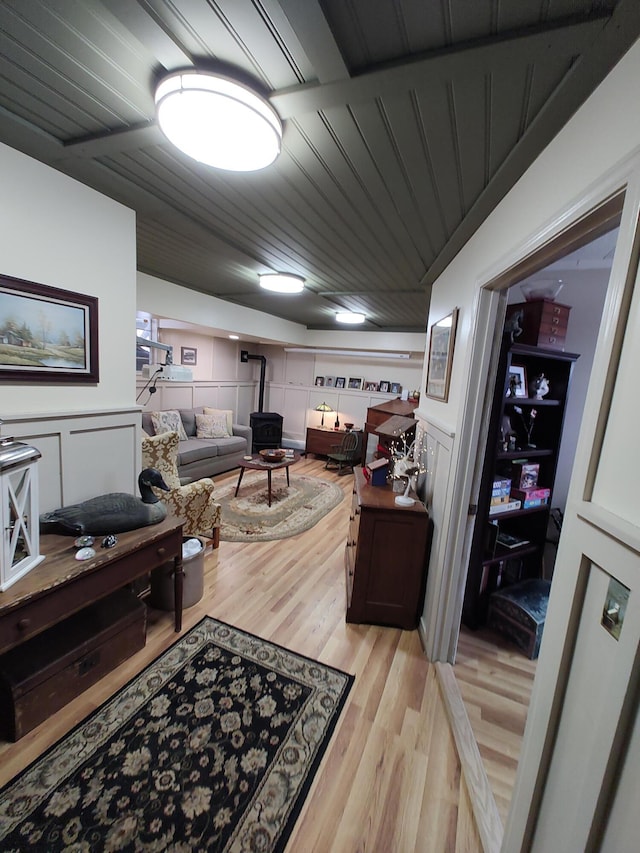 office with wood ceiling, a decorative wall, a wood stove, and light wood-style floors