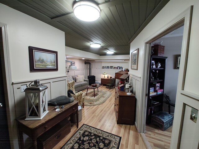 living area with wooden ceiling, a decorative wall, a wainscoted wall, light wood finished floors, and a wood stove