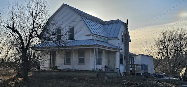 view of front facade with covered porch, a gambrel roof, metal roof, and a standing seam roof