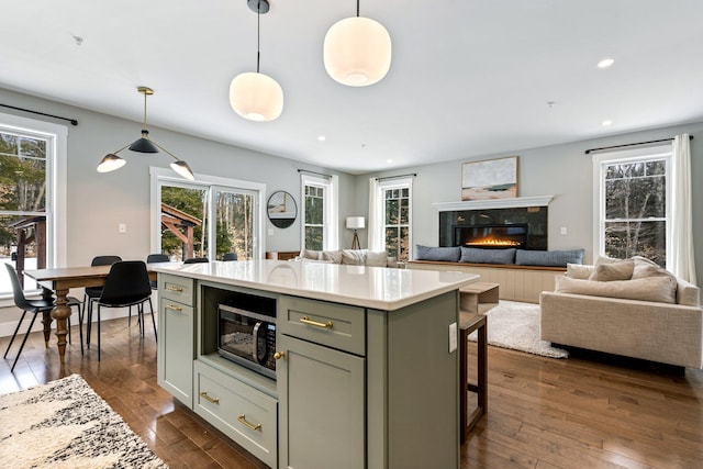 kitchen with dark wood-style floors, recessed lighting, light countertops, a glass covered fireplace, and stainless steel microwave