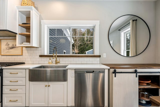 kitchen featuring a sink, backsplash, dishwasher, light countertops, and open shelves