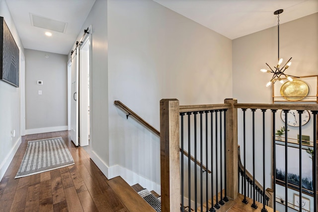 staircase featuring hardwood / wood-style floors, visible vents, baseboards, a barn door, and a notable chandelier