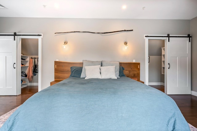 bedroom with a walk in closet, baseboards, a barn door, wood finished floors, and a closet