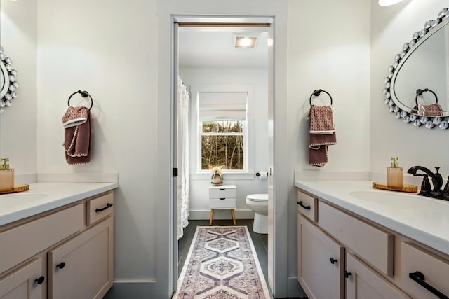 bathroom with a sink, toilet, and two vanities