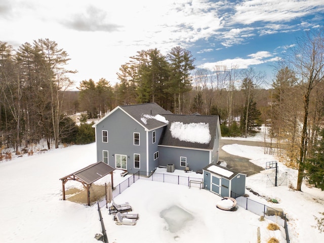 snow covered back of property with a shed, an outdoor structure, and fence