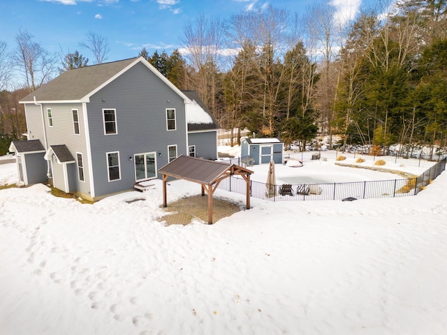 snow covered rear of property featuring an outbuilding, a storage unit, and fence