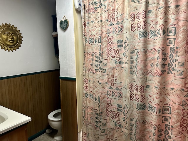 bathroom with toilet, wainscoting, wood walls, vanity, and a shower with curtain