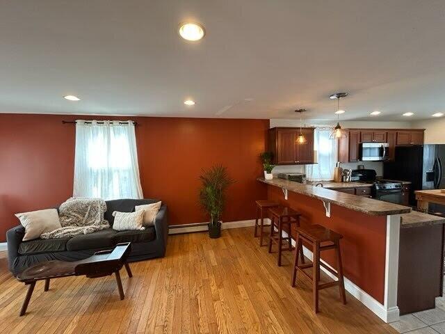 kitchen featuring range with gas stovetop, a breakfast bar area, stainless steel microwave, a baseboard heating unit, and a peninsula