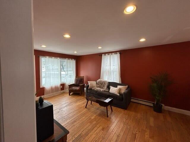 living room with light wood finished floors, baseboard heating, and a healthy amount of sunlight