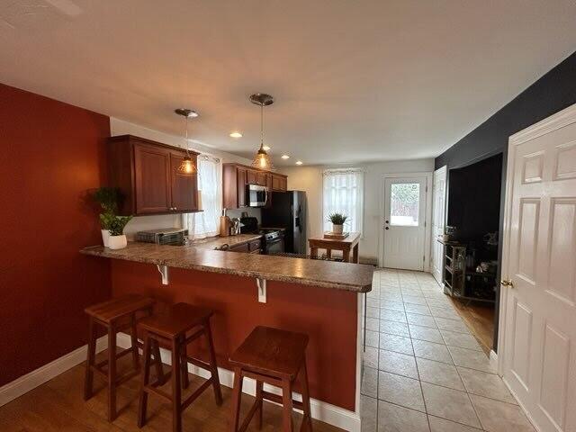 kitchen with brown cabinets, decorative light fixtures, stainless steel appliances, a peninsula, and a kitchen breakfast bar