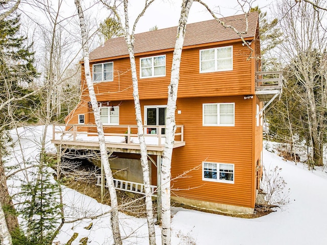 snow covered property with a shingled roof