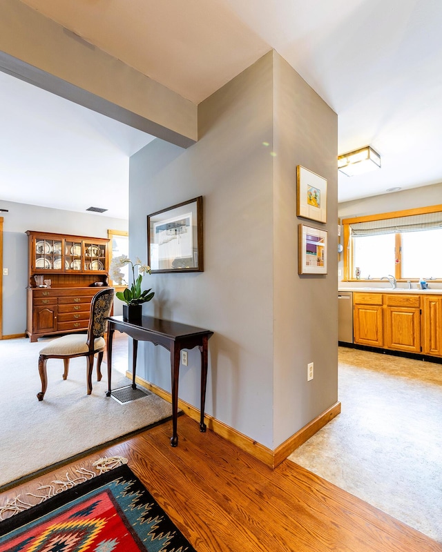 hall featuring light wood finished floors, baseboards, visible vents, light colored carpet, and a sink