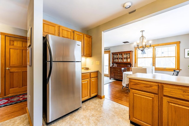 kitchen with visible vents, brown cabinets, freestanding refrigerator, light countertops, and a chandelier