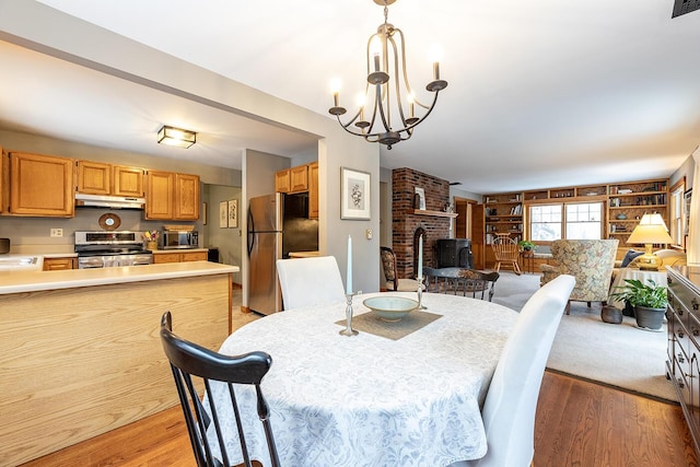 dining space with a brick fireplace, light wood finished floors, and an inviting chandelier