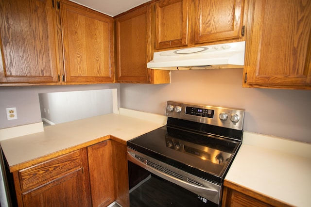 kitchen featuring brown cabinetry, ventilation hood, stainless steel electric range oven, and light countertops