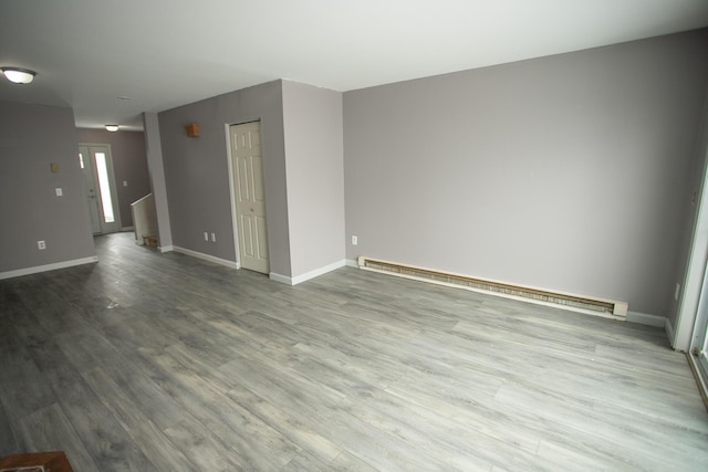 empty room featuring a baseboard heating unit, wood finished floors, and baseboards