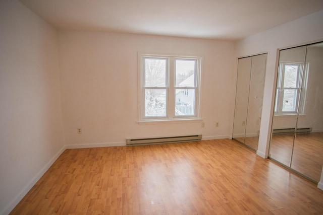 unfurnished bedroom with light wood-type flooring, a baseboard heating unit, multiple closets, and multiple windows