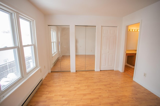 unfurnished bedroom with two closets, connected bathroom, baseboard heating, and light wood finished floors