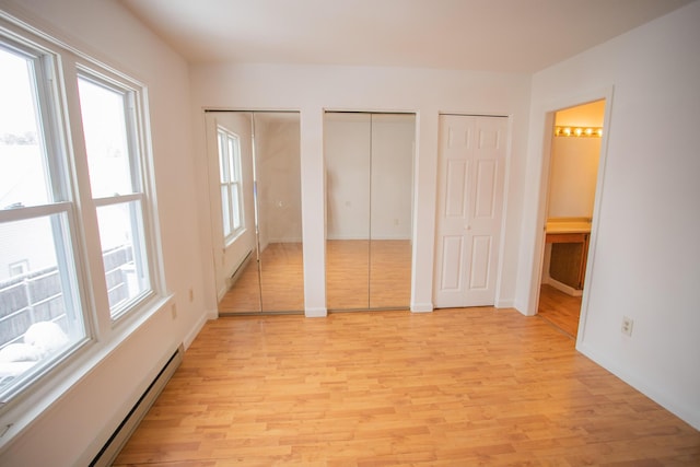 unfurnished bedroom with multiple closets, baseboard heating, ensuite bath, and light wood finished floors