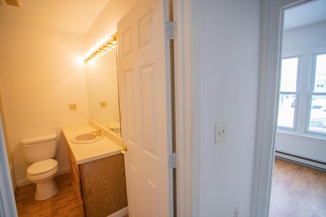 half bath with vanity, wood finished floors, baseboards, toilet, and baseboard heating