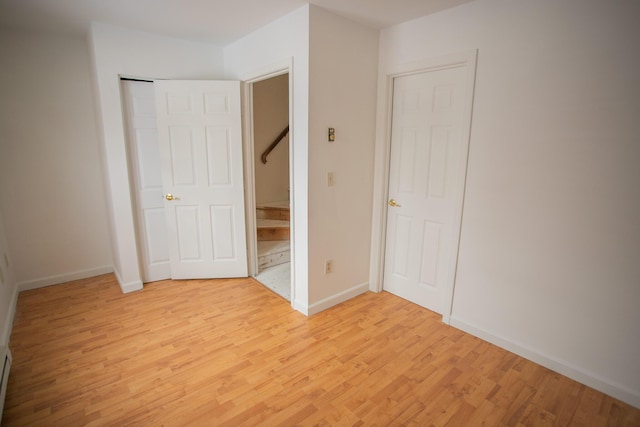 unfurnished bedroom with light wood-type flooring, baseboards, and a baseboard heating unit