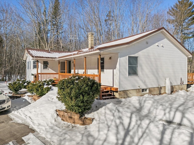 snow covered rear of property with a porch, a chimney, and metal roof